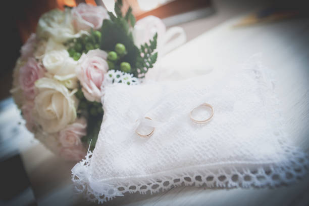 istock Wedding rings on white pillow with bouquet 942809840