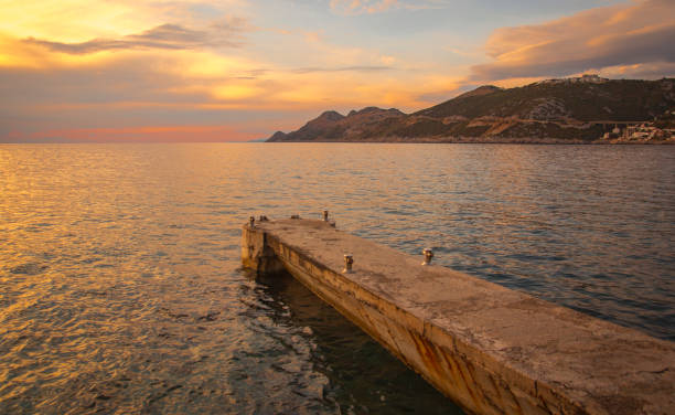 istock Cloudy sunset with mountains and docks at sea 942825000