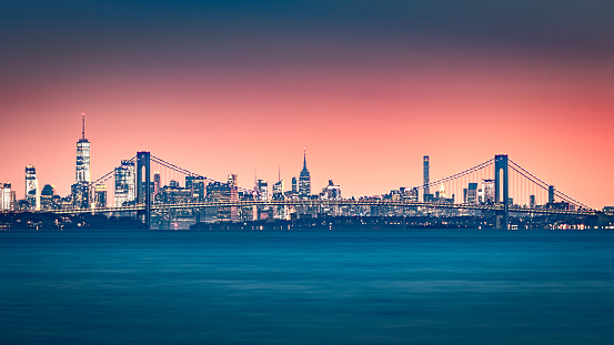 Verrazano Narrows Bridge gates the access to Upper New York Bay. Manhattan skyline rises behind the bridge