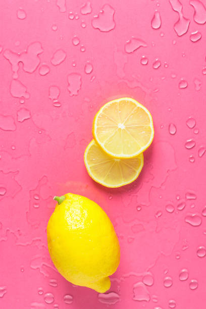 Ripe Juicy Whole and Sliced Lemon on Fuchsia Pink Background with Water Drops. Vitamins Healthy Diet Summer Superfoods Concept. Poster Banner Template. Copy Space Flat Lay