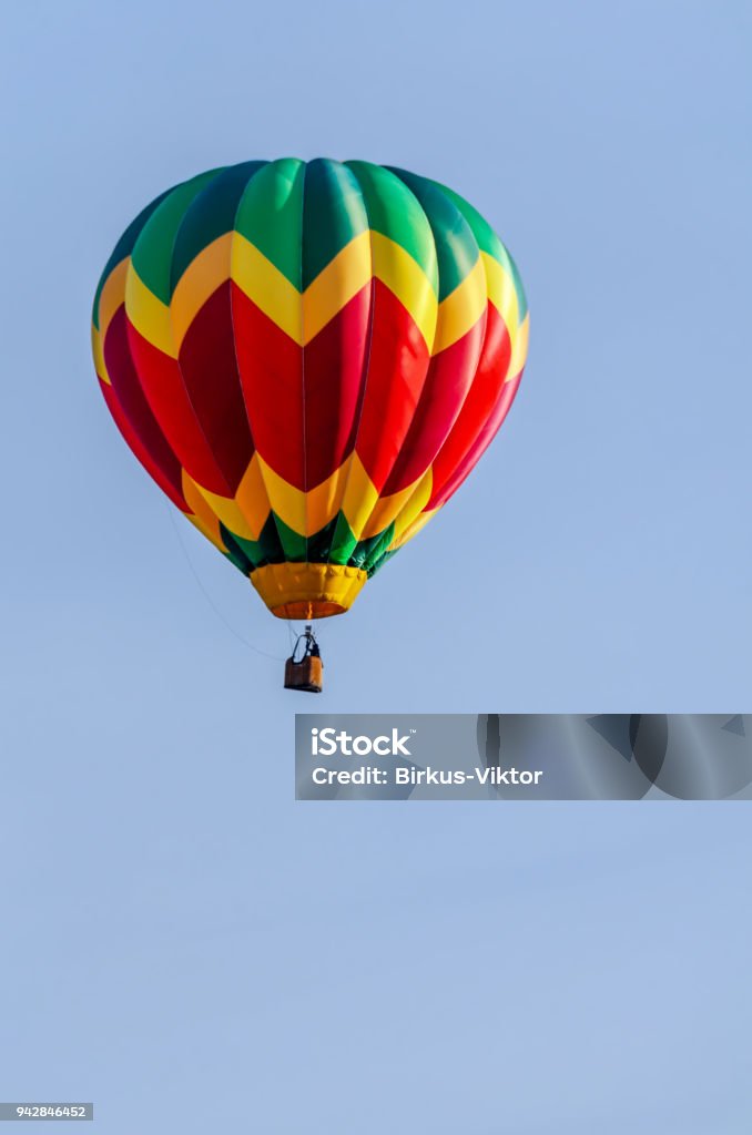 colorful balloon with a basket flies in a blue sky a colorful balloon with a basket, a flame of fire and a silhouette of a pilot flies in a blue sky Adventure Stock Photo