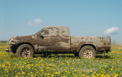 Extended cab truck covers in mud sitting in a meadow