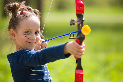 Cute girl archer with bow shooting in sunny summer day. little girl shoots bow in the park. Outdoors. Sport activities with children. Sport and lifestyle concept. Aiming high