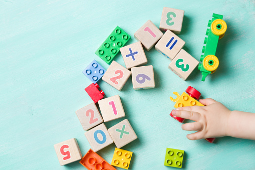 Niño jugando con cubos de madera con números y ladrillos del juguete colorido sobre un fondo de madera color turquesa. Números de aprendizaje del niño. Mano de un niño que toma los juguetes. photo