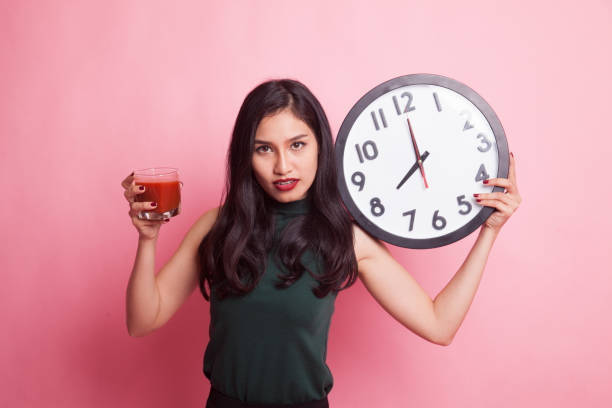 istock Young Asian woman with tomato juice and clock. 942875096