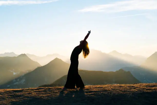 She is bending backwards as sun rises behind her.  She is in an open meadow, Ticino Canton