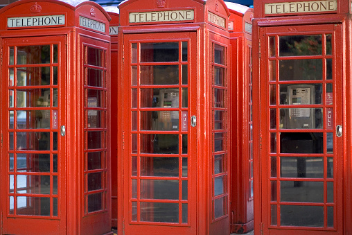 A telephone box that once had a paid telephone, is rewired with a standard telephone that is set in rural scene near railroad tracks along a dirt road on a sunny day.