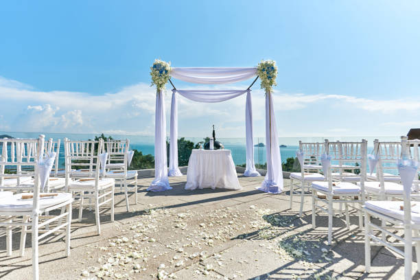 Wedding venue setting, Arch and altar decorated with roses, flowers, ocean background The wedding arch, altar setup with white table, The one big and two small candle use for decoration on the white table with fabric cover. The marriage license on the table, panoramic ocean view. phuket beach party stock pictures, royalty-free photos & images