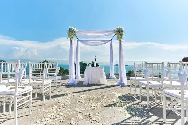 The wedding arch, altar setup with white table, The one big and two small candle use for decoration on the white table with fabric cover. The marriage license on the table, panoramic ocean view.