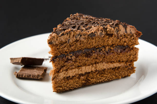 istock Chocolate cake with chocolate slices and sprinkling served on a white plate on a black background 942926594