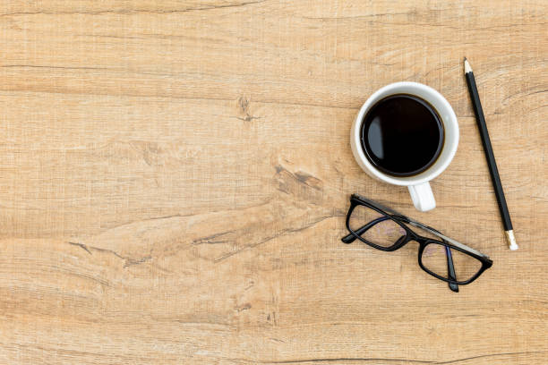 istock Wood desk table with coffee, eye glasses and pencil. Top view with copy space, flat lay. 942926836