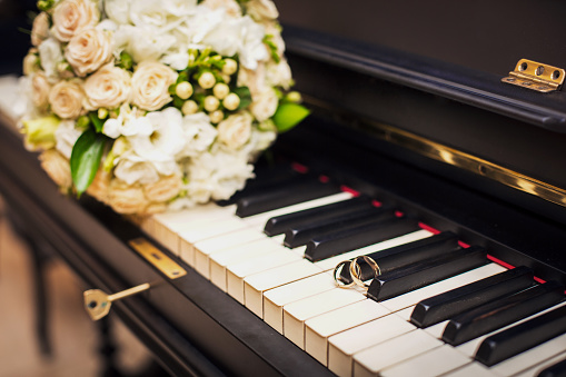 golden wedding rings and flower bouqet lie on the piano