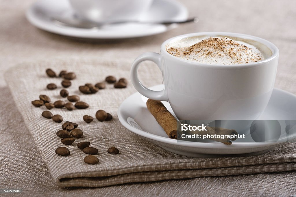 A cup full of cappuccino surrounded by coffee beans Chill out and leisure concept. Freshly prepared cup of italian cappuccino with rich milk foam sprinkled with cinnamon. Cafe Stock Photo