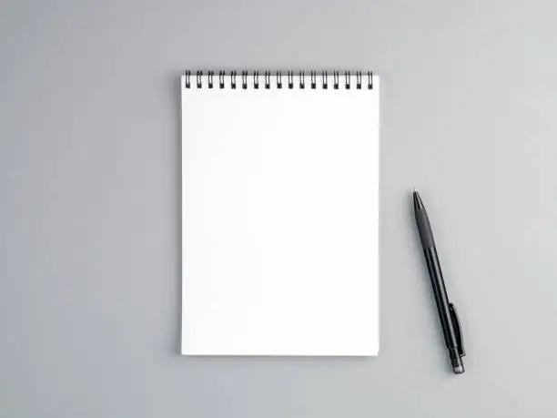 blank sheet of notebook with a spiral and pen on a neutral gray textured  background