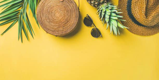 Colorful summer female fashion outfit over yellow background, wide composition Colorful summer female fashion outfit flat-lay. Straw hat, bamboo bag, sunglasses, palm branches, pineapple over yellow background, top view, copy space, wide composition. Summer fashion, holiday concept beach bag stock pictures, royalty-free photos & images