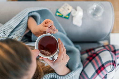 Upper view of Sick woman with a headache sitting on a sofa at home wrapped in blanket during the day. Sickness, seasonal virus problem concept. Woman being sick having flu lying on sofa.