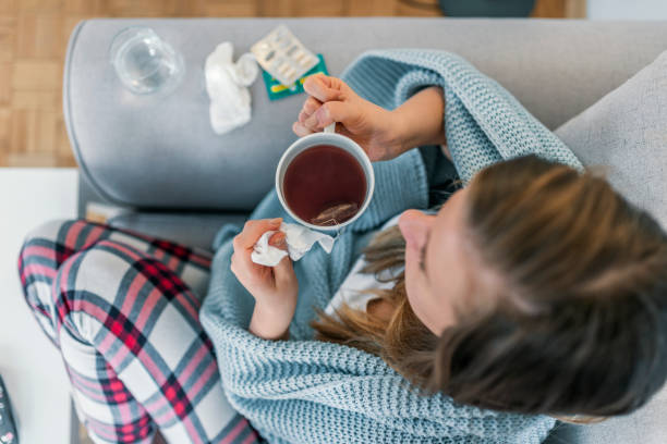 Sick young woman in the bed having hot drink