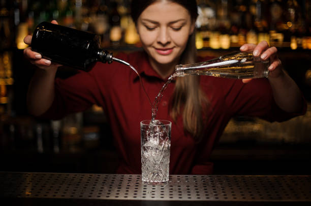 young female bartender poting gin and sweet syrup into a glass - drink on top of ice food imagens e fotografias de stock
