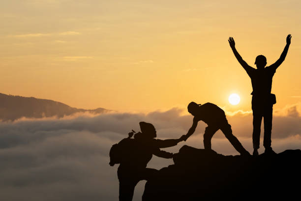 freunde helfen einander und mit teamwork, die versuchen, auf dem gipfel der berge im schönen sommer sonnenuntergang. - rescue mountain horizontal three people stock-fotos und bilder