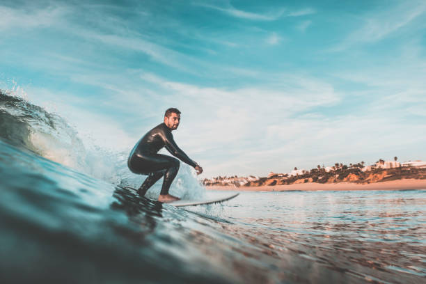 hombre joven atractivo surfeando una ola de la costa - surf fotografías e imágenes de stock