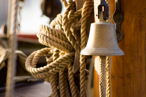 Atmospheric brass ships bell against wooden mast with natural fibre ropes and wooden tackle blocks. Adobe RGB 1998 color profile.