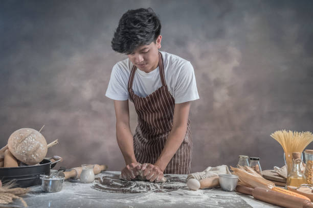 istock Man preparing buns at table in bakery, Man sprinkling flour over fresh dough on kitchen table 942948970