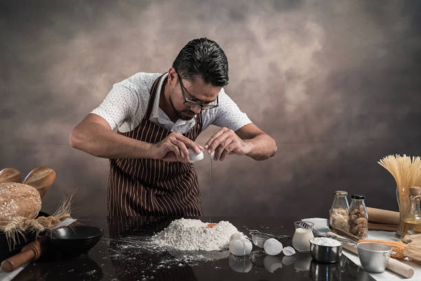 istock Man preparing buns at table in bakery, Man sprinkling flour over fresh dough on kitchen table 942949162