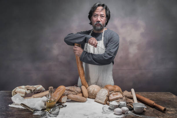 istock Man preparing buns at table in bakery, Man sprinkling flour over fresh dough on kitchen table 942949454