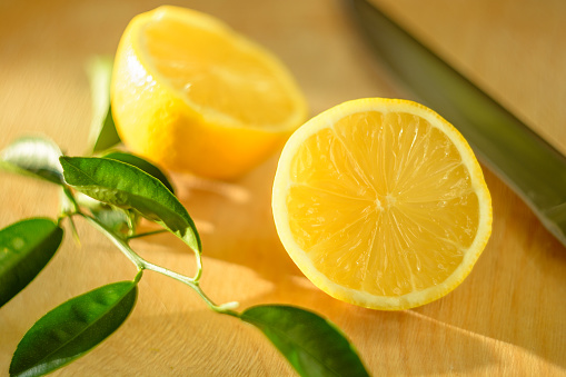 Cut lemon with green leaves and a knife on a wooden board lit by the sun