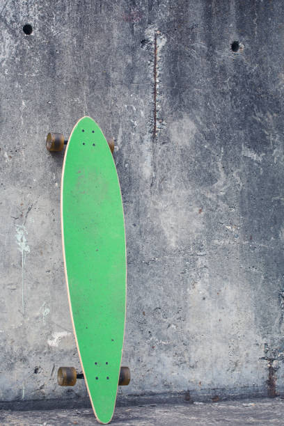 istock Green longboard against a rough concrete wall. 942966276