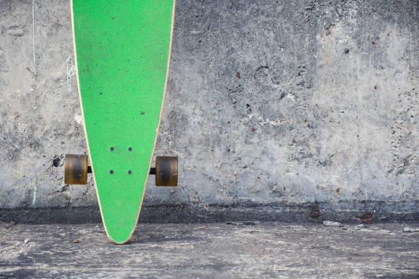 istock Green longboard against a rough concrete wall. 942966334