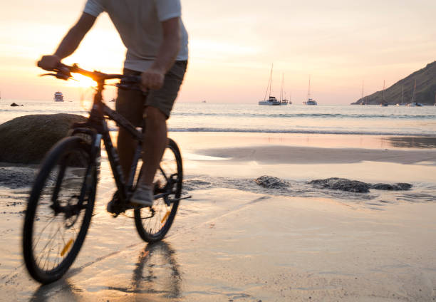 istock Man cycles across wet sand at sunset 942971994