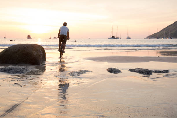 istock Man cycles across wet sand at sunset 942972116