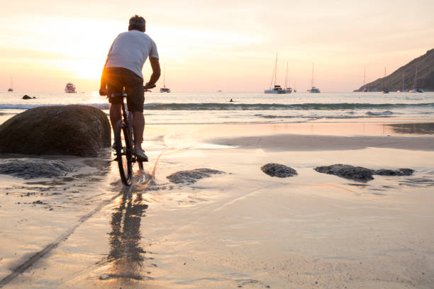 istock Man cycles across wet sand at sunset 942972332