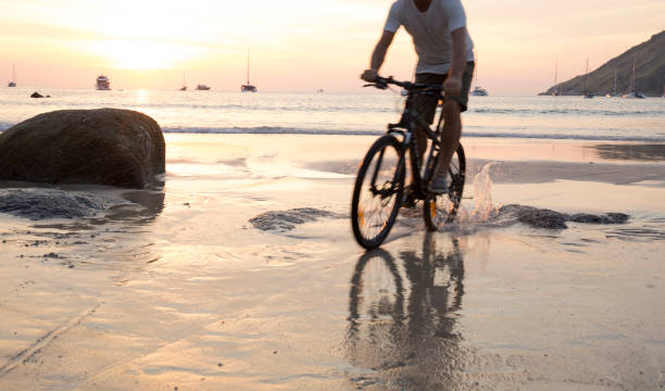 istock Man cycles across wet sand at sunset 942972480