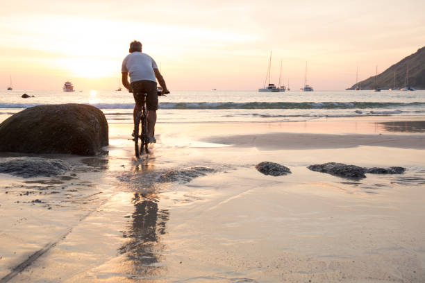 Man cycles across wet sand at sunset