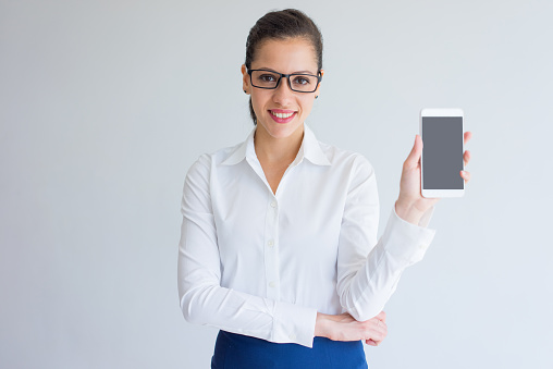 Happy excited young female business specialist showing smarphone screen. Cheerful beautiful Caucasian businesswoman looking at camera. Gadget concept