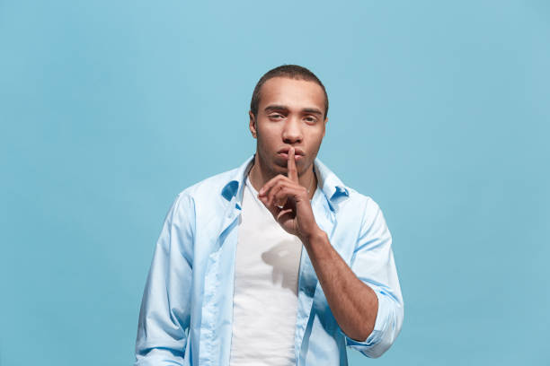 istock The young man whispering a secret behind her hand over blue background 942988366