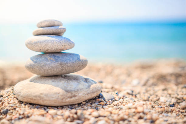 istock Stones are lined with pyramid on beach. Pebbles. Stones pyramid symbolizing zen, harmony, balance on ocean background. pebble stack on sea coast line. Stones on beach against blue sea in summer day. 942992214
