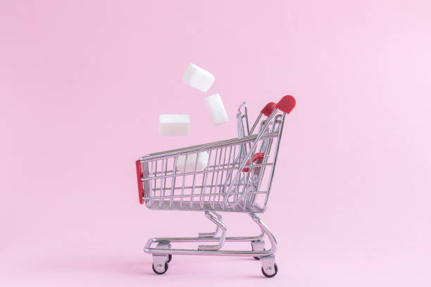 Shopping trolley with sugar cubes isolated on rose minimalistic concept.