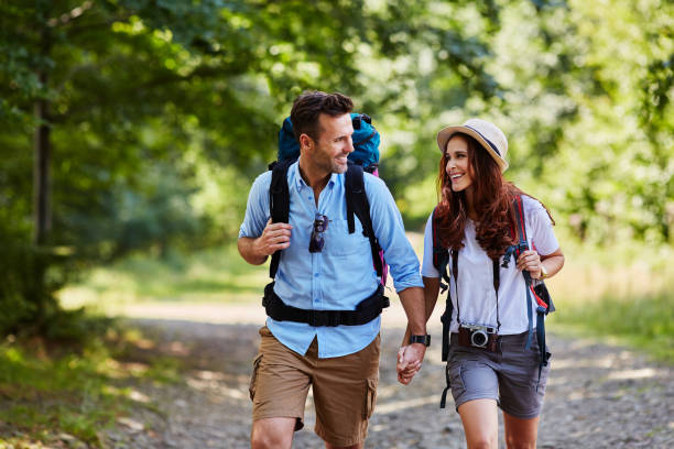 happy couple hiking together in mountains with backpacks - nature forest clothing smiling imagens e fotografias de stock
