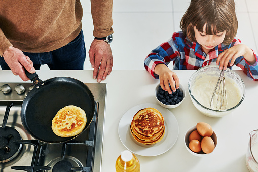 High angle shot of an adorable little boy making pancakes with his unrecognizable father in the kitchen at home