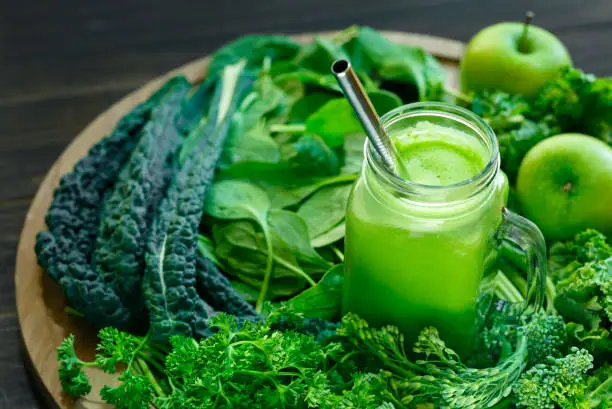 Variety of fresh organic leafy greens with a glass jar of juice with a sliver drinking straw