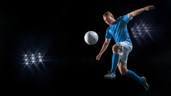 Male football player kicking ball in air at night.