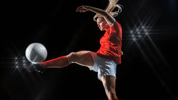 Female footballer kicking ball Female football player kicking ball against black background. football socks stock pictures, royalty-free photos & images