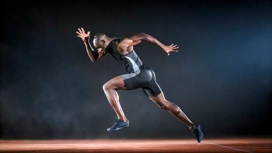 Male sprinter running on track at night.