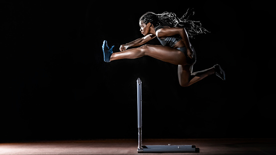 Female sprinter jumping over hurdle on track.