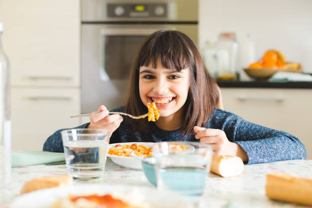Delicious pasta for kids Cute and happy little girl eating pasta with tomato sauce and powdered cheese in the kitchen at home kids eating noodles stock pictures, royalty-free photos & images