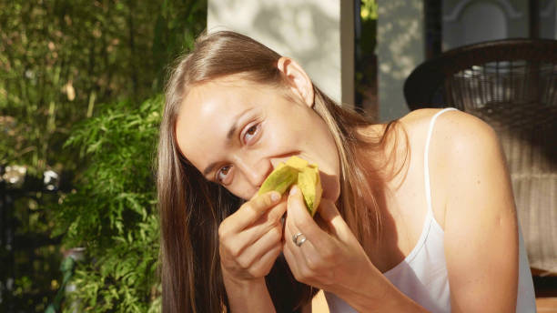 Portrait of happy young woman eats mango with pleasure at green garden stock photo