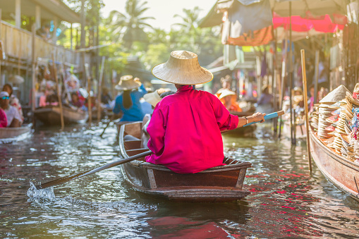 Damnoen Saduak Floating Market, Thailand - November 29, 2015:   At the famous Damnoen Saduak Floating Market locals sell their fresh products (fruits and vegetables) aboard small wooden boats. It's a unique shopping experience.  Hats and colorfull umbrellas allow sellers to protect themselves from the country's warm sun.